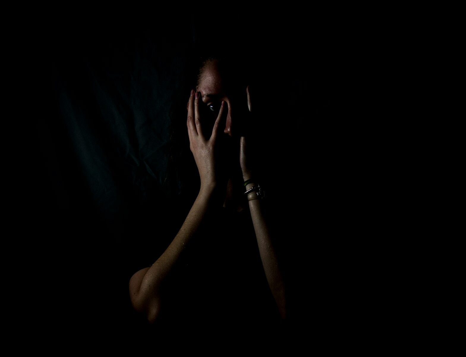 Photo by Melanie Wasser woman holding her face in dark room